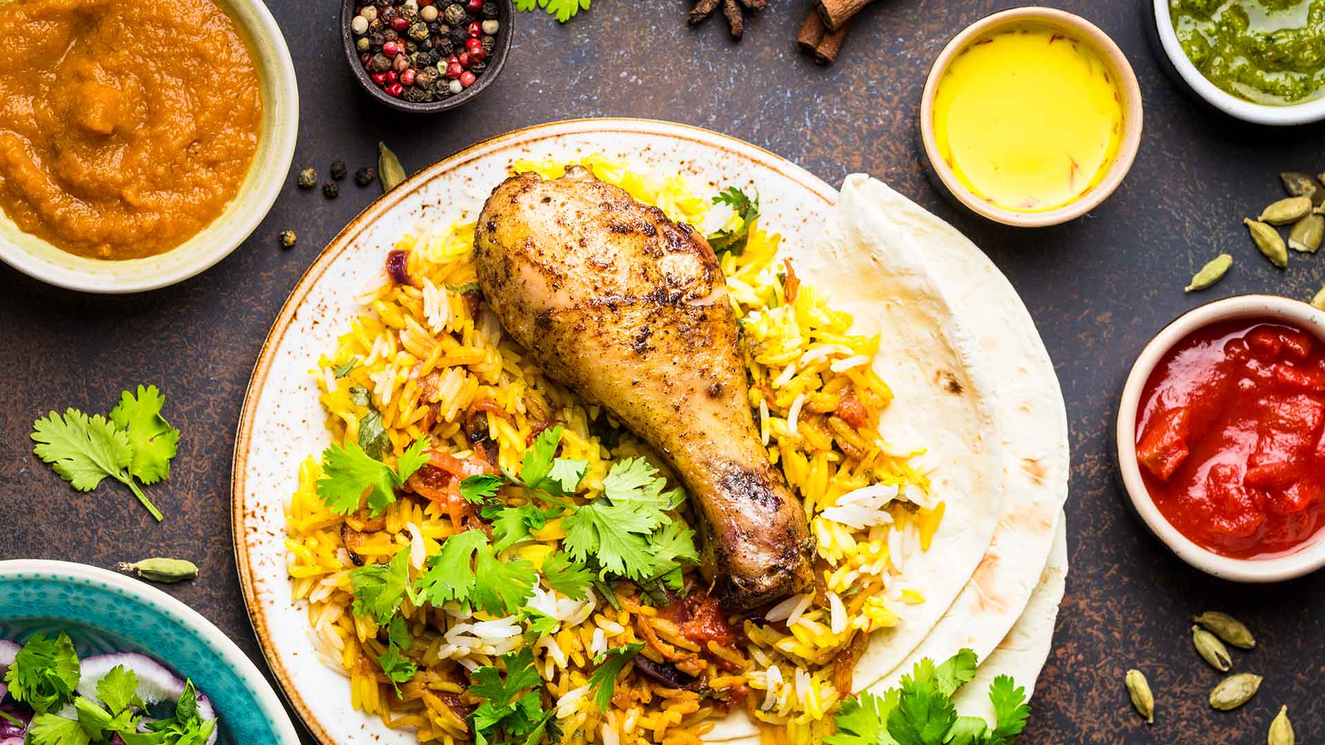 A table spread with chicken biryani, condiments, and side dishes