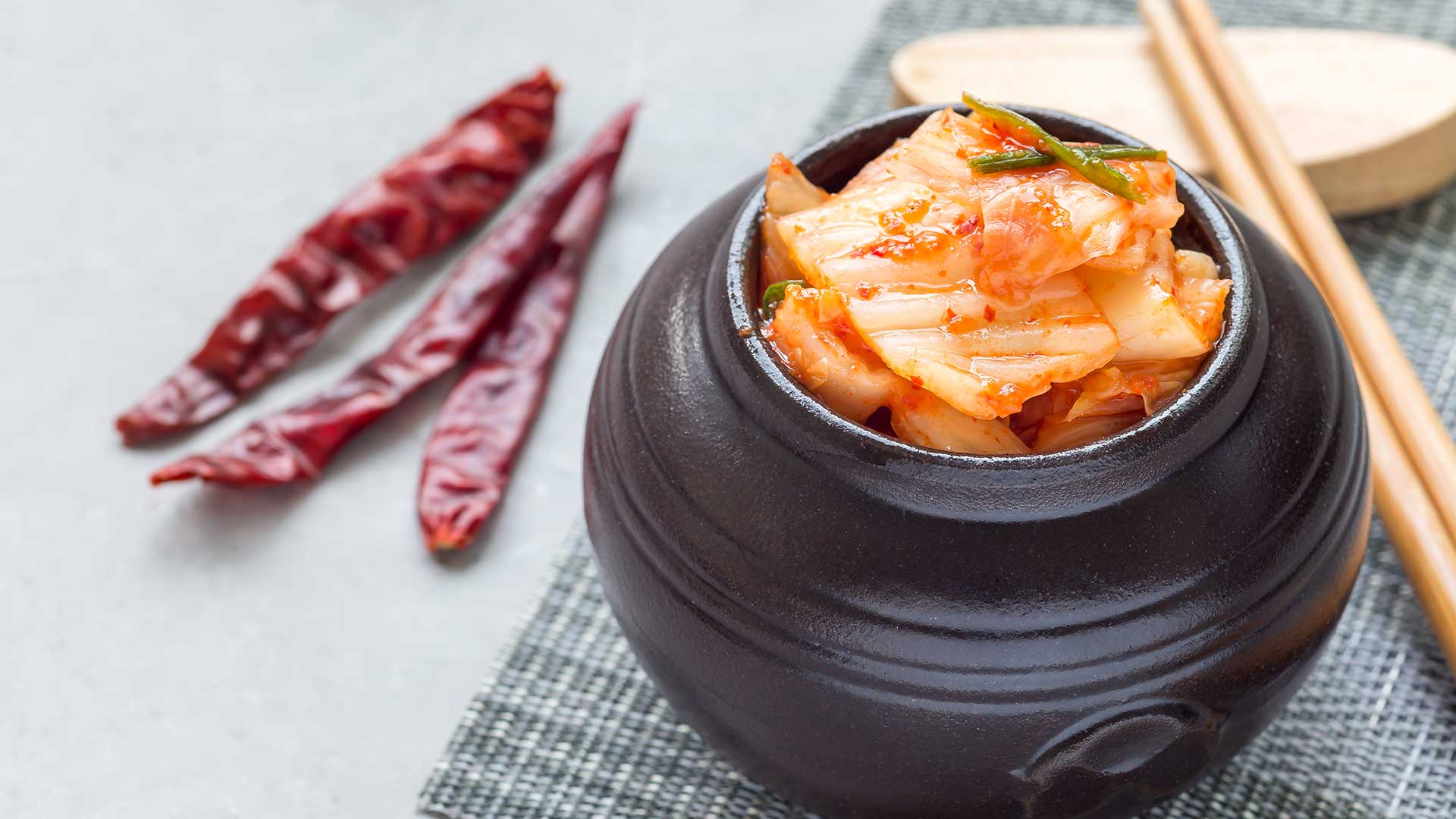 A pot of kimchi on a table with chopsticks and chilis