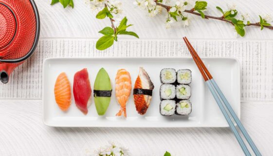 A plate of assorted sushi with chopsticks on a white table